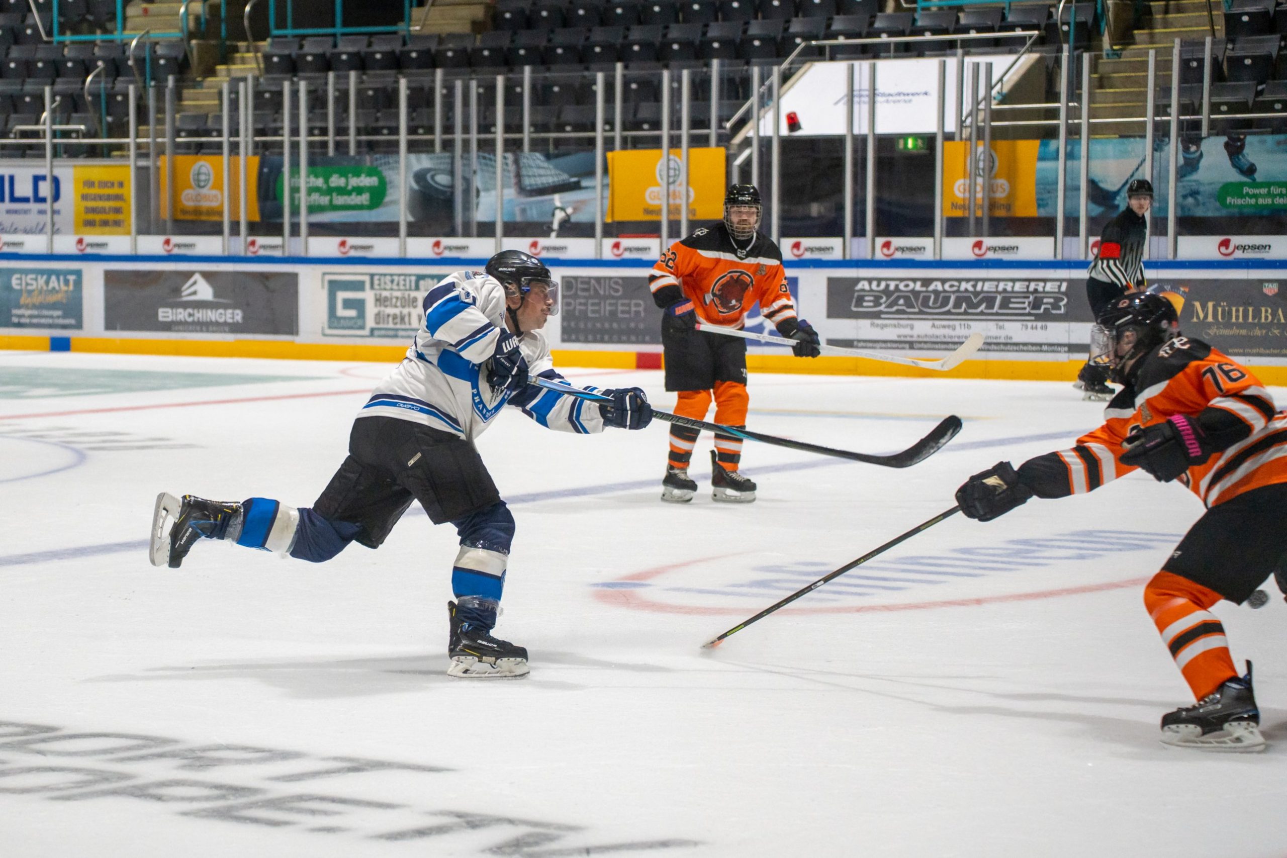 Spieler der EHC Regensburg Phantoms holt zu einem Schuss aus, zwei Gegner in Orange verteidigen
