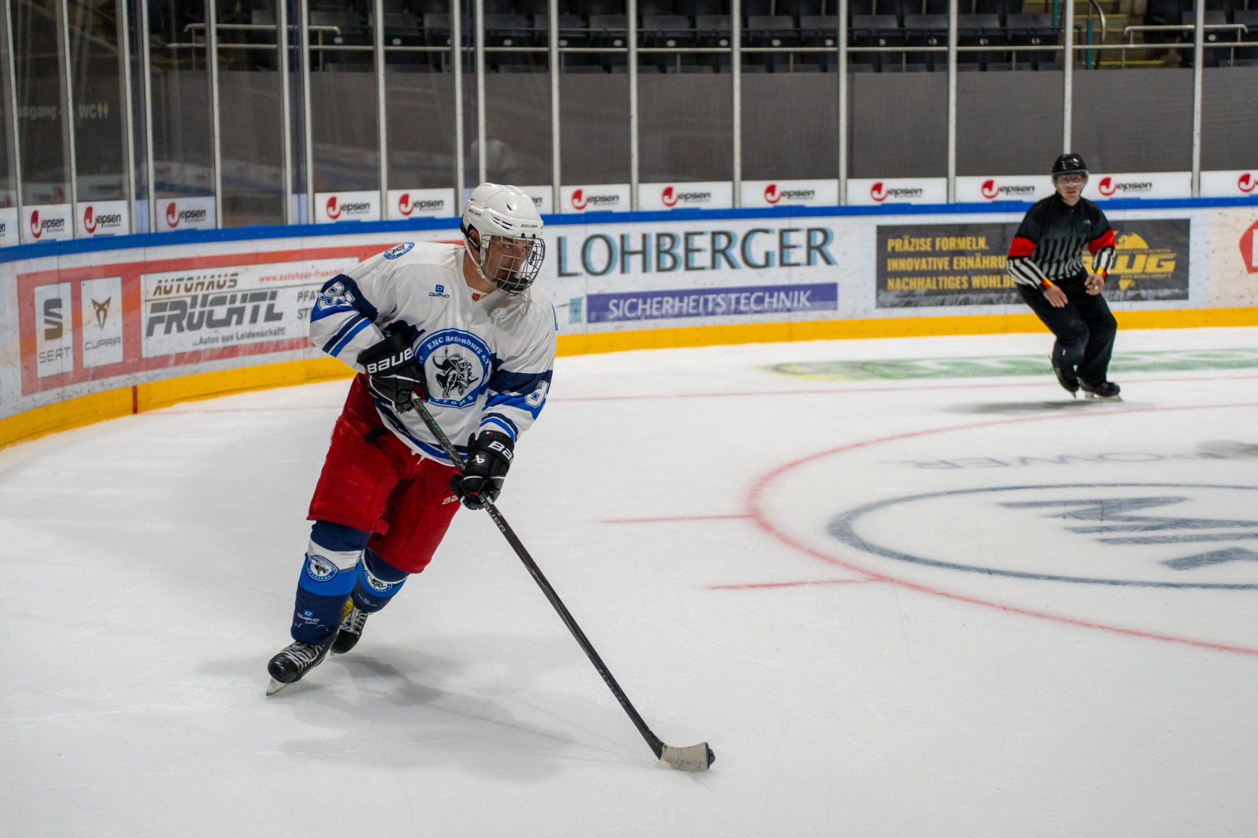 Spieler der EHC Regensburg Phantoms führt den Puck durch das Drittel, ein Schiedsrichter folgt
