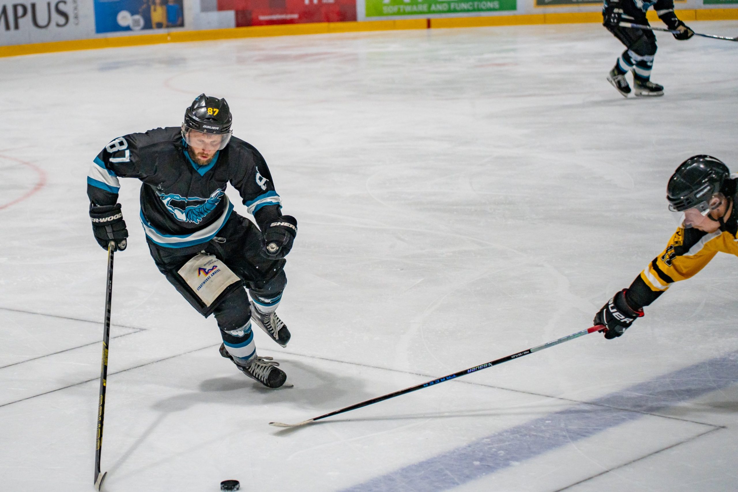 Spieler in dunklem Trikot läuft mit dem Puck, ein Gegner streckt den Schläger nach ihm aus